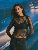 Top de encaje negro con diseño floral, manga larga y cuello redondo. Presenta un acabado festoneado en el ruedo y mangas.