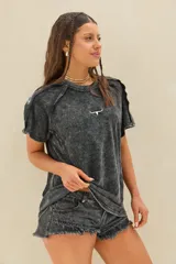 Remera oversize de manga corta en color negro con efecto acid wash. Presenta un pequeño logo blanco bordado en el centro del pecho y detalles de costuras expuestas en los hombros.