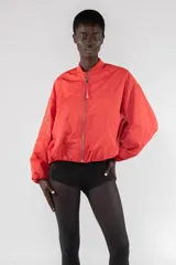 Campera bomber color rojo anaranjado de nailon repelente al agua, corte regular, cierre frontal con cremallera visible, tirador con logo bordado, bolsillos de ribete verticales, hombro caído, bolsillo utilitario con cremallera en la manga, cuello de chaqueta bomber acanalado y puños y bajo elásticos fruncidos.