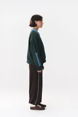 Buzo estilo rugby de corte oversized, color verde oscuro, con cuello tipo camisa en denim azul claro y cierre frontal parcial. Presenta un recorte horizontal en el pecho, logo bordado y tiras laterales en las mangas en contraste.