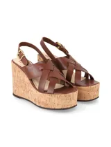 Sandalias de plataforma con taco acuñado de corcho y tiras cruzadas de cuero marrón en el empeine, con tira ajustable al talón y hebilla metálica dorada.