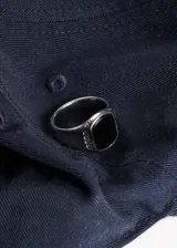 Anillo plateado de acero quirúrgico con piedra negra rectangular en el centro y diseño de grecas en los laterales.