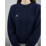 Sweater de punto color crema con diseño de trenzas y rombos, cuello redondo y mangas largas. Presenta un pequeño aplique decorativo en el pecho.