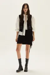 Chaleco de cuero negro con flecos largos en los laterales y detalles bordados en hilo blanco en la espalda.