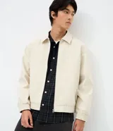 Campera boxy de poliéster color beige, con cuello inglés, cierre frontal de cremallera, mangas largas con elástico en los puños, bolsillos laterales y detalles de recortes.