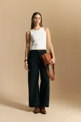 Jean de corte wide leg y tiro alto, color negro con costuras en contraste color ocre. Presenta bolsillos delanteros y traseros con detalle de pespunte, y ruedo ancho con costura decorativa.