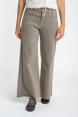 Jean de corte wide leg y tiro medio, en color gris topo. Presenta un diseño de pierna ancha con ruedo desflecado y cierre frontal con botón y cremallera.