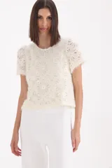 Sweater de punto de textura suave en color crudo, con diseño de flores bordadas y lentejuelas aplicadas. Presenta cuello redondo y mangas cortas, con un corte recto y holgado.