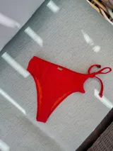 Parte inferior de bikini tiro alto, estilo colaless, color azul eléctrico con textura gofrada. Presenta lazos ajustables laterales con punteras decorativas de resina verde.