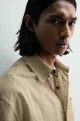 Camisa de hombre de manga larga, color beige con micro-estampado a cuadros en tonos marrones. Presenta cuello solapa abotonado (button-down), un bolsillo de parche en el pecho y cierre frontal de botonadura.