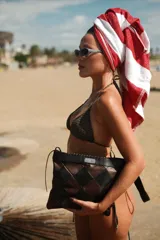 Sobre estructurado con diseño de rombos entrelazados en tonos marrón y negro. Presenta una placa metálica con logo en la parte superior y cierre superior.