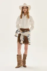 Camisa blanca de corte recto, con cuello clásico y mangas largas abullonadas que presentan detalles en punto smock en los puños. Incluye un pequeño bordado en el pecho.