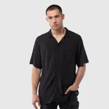 Camisa de manga corta confeccionada en viscosa, con cuello solapa y cierre frontal de botones. Presenta un diseño con estampado de cuadros tono sobre tono y un bolsillo frontal en el pecho.