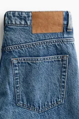 Jean de tiro alto confeccionado en denim de algodón lavado con diseño de cinco bolsillos, piernas rectas y holgadas, y detalles de roturas en las rodillas.