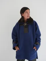 Buzo azul con cuello de piel sintética marrón, detalle de cuero sintético negro con hebilla dorada en el pecho y puños con hebillas.