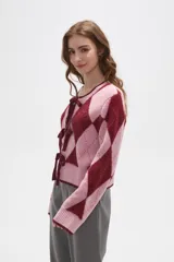 Cardigan de punto con diseño de rombos en tonos rosa y bordó. Presenta cierre frontal mediante lazos anudados, cuello redondo y mangas largas con puños acanalados.