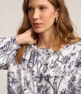 Blusa blanca estampada con flores azules, de mangas largas abullonadas con puños ajustados y volado en el cuello.