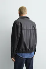 Cazadora bomber de efecto piel color marrón oscuro, con cuello solapa, cierre frontal de cremallera, bolsillos de vivo en cadera y bajo elástico.