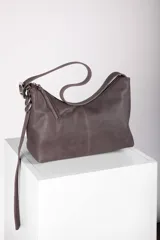 Bandolera Aliada de cuero gris oscuro, con diseño descontracturado, cierre metálico, bolsillo interior y correa ancha regulable con hebilla y argollas metálicas.
