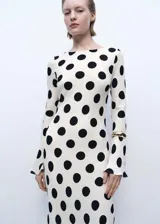 Vestido largo color crema con estampado de lunares negros, de corte ajustado, cuello redondo y mangas largas acampanadas.