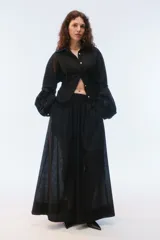 Camisa oversize negra de algodón liviano con textura calada, cuello camisero, botones frontales, mangas largas voluminosas y tiras para anudar en la espalda.