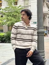 Buzo tejido de punto con diseño a rayas horizontales en color beige y marrón. Presenta cuello tipo polo con cierre frontal parcial y puños acanalados.
