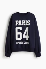 Buzo azul marino de corte oversized con cuello redondo ribeteado acanalado y diseño de texto blanco estampado en el frente que dice 'Paris 64 Sports Club'. Modelo con hombros caídos y remate acanalado en puños y bajo. Interior cepillado suave.