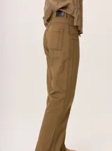 Jean recto de gabardina color marrón verdoso (camel/oliva), con costuras y atraques en hilo negro contrastante. Presenta un pequeño detalle bordado en rojo en el bolsillo trasero.