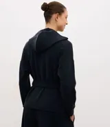Campera deportiva de estilo utilitario color negro, confeccionada en tejido técnico. Presenta capucha, cierre frontal con botones, bolsillos con solapa en el pecho y lazo ajustable en la cintura. Posee mangas largas con puños y diseño liso.