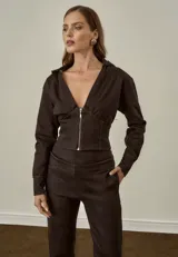 Chaqueta marrón con cuello camisero, mangas largas y cierre frontal con cremallera. Presenta un diseño ajustado al cuerpo con efecto corsé.