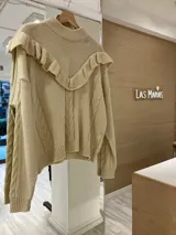 Sweater color beige de tejido de punto con ochos, cuello alto y volados en el escote.
