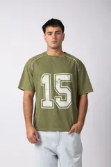 Remera de algodón con efecto lavado gastado en color verde oliva, con estampado frontal del número 15 en color blanco y detalles de costuras blancas en los hombros.