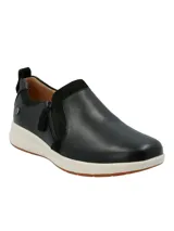 Zapatilla tipo slip-on Hush Puppies modelo Spinal, confeccionada en cuero negro con detalles en gamuza y cierre lateral. Cuenta con una suela de goma blanca con base antideslizante y tecnología de amortiguación.