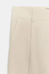 Pantalón gris de tiro alto con bolsillos delanteros y traseros, detalle de pliegues frontales y cierre frontal con cremallera y botón.