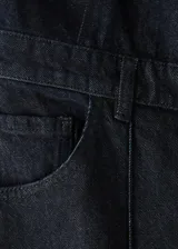Mono largo de denim color negro, con cierre frontal de botones metálicos, bolsillos frontales y traseros, y perneras de corte recto.