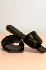 Sandalias planas negras con tiras anchas trenzadas y suela marrón.