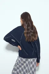 Sweater de tejido suave color marrón con diseño de líneas bordadas en color rojo. Presenta cuello redondo, manga larga y calce relajado.