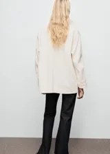Anorak de estilo utilitario en color crudo, con cuello alto tipo embudo, cierre frontal con cremallera y botones a presión, y múltiples bolsillos de parche con solapa. Presenta un diseño oversize de manga larga.