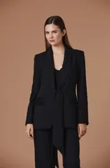 Blazer negro entallado de diseño estructurado, con cuello smoking, cierre de lazo frontal y detalles de encaje bordado con apliques de brillo en las mangas y en las solapas de los bolsillos.