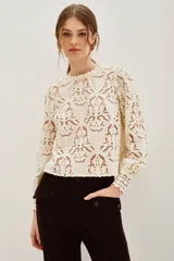 Camisa de encaje negro con cuello alto y mangas largas abullonadas. Presenta un diseño calado con motivos florales y cierre posterior.