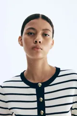 Cárdigan corto de punto acanalado en mezcla de viscosa, con rayas horizontales blancas y azul marino. Presenta cuello redondo ribeteado en azul marino, cierre frontal con botones dorados y bolsillos insertados decorativos con botón dorado. Tiene mangas cortas.