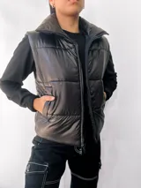 Chaleco puffer negro con cuello alto y cierre frontal con cremallera. Tiene bolsillos laterales y diseño acolchado.