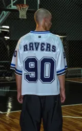 Camiseta estilo jersey de fútbol americano, color blanco, con cuello en V ribeteado en azul. Presenta el número "90" grande en el frente en azul marino con borde blanco. Tiene bordados en el pecho como "Lx." y "Ravers", y números pequeños en las mangas. Los puños tienen franjas azules y negras.