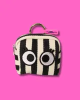 Bolsita cuadrada de tela con estampado de rayas verticales verdes y blancas, decorada con un aplique bordado de ojos grandes. Cuenta con cierre superior y una argolla metálica para colgar.