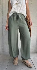 Pantalón tipo babucha de color verde militar, con cintura elástica fruncida y cordón ajustable. Cuenta con diseño amplio y puños elásticos en los tobillos.