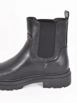 Bota tipo Chelsea de caña media, confeccionada en cuero sintético negro con paneles elásticos laterales y suela track dentada.