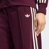 Pantalón deportivo Adidas Firebird de corte holgado, color bordó con las icónicas tres rayas laterales en blanco y logo del trébol bordado. Presenta cintura de tiro medio y diseño de pierna ancha.