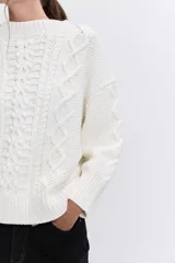 Sweater de punto color blanco off-white, con cuello redondo y diseño texturizado con trenzas y pompones en el frente.