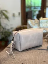 Neceser de cuero con acabado brillante, cierre superior y tirador de cuero con detalle de cinta estampada.