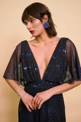 Vestido largo negro con brillos azules, escote en V pronunciado, mangas cortas y amplias tipo capa, y corte en la cintura.